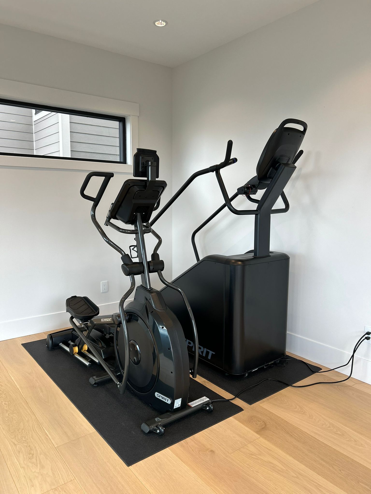 Spirit elliptical and stair climber cardio corner on rubber mats over hardwood, custom indoor home gym in Abbotsford, BC