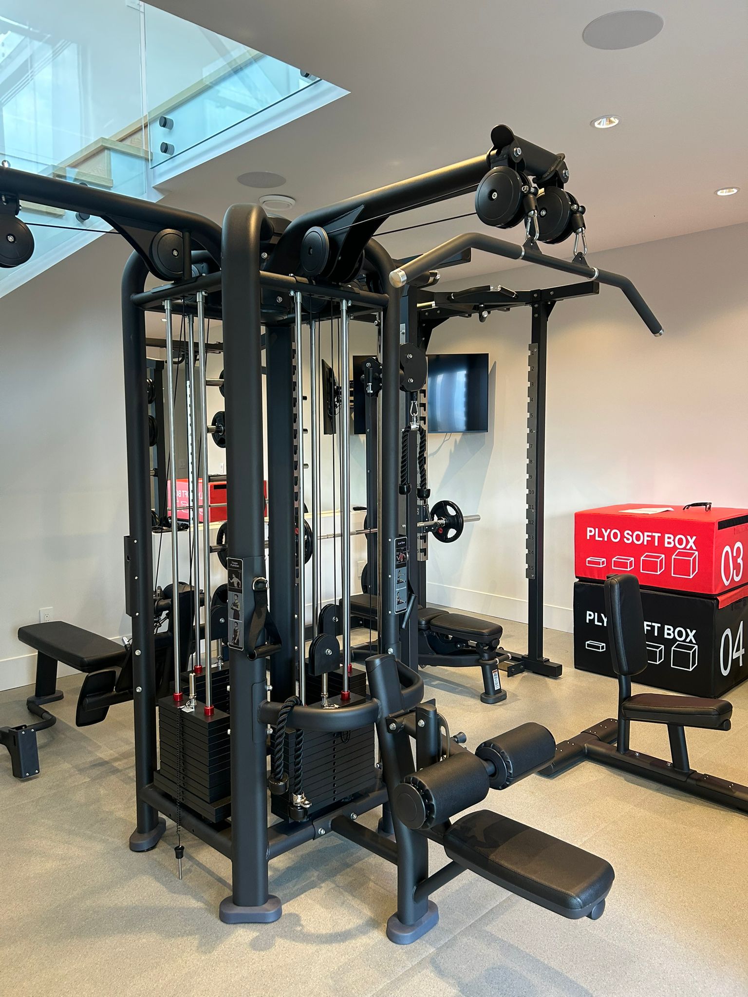 Custom indoor home gym in Abbotsford, BC with a multi-station cable machine, power rack, benches, and soft plyometric boxes
