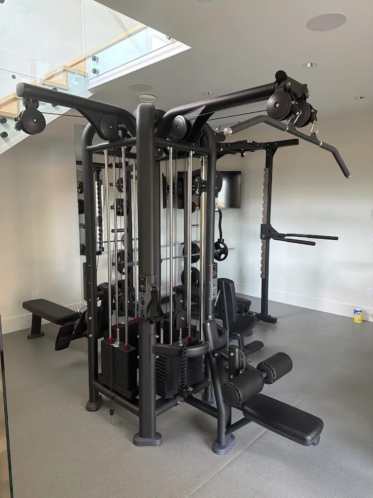 Custom indoor home gym build in Abbotsford, BC — four-station cable machine, squat rack, and adjustable bench in a modern white-walled room with skylight