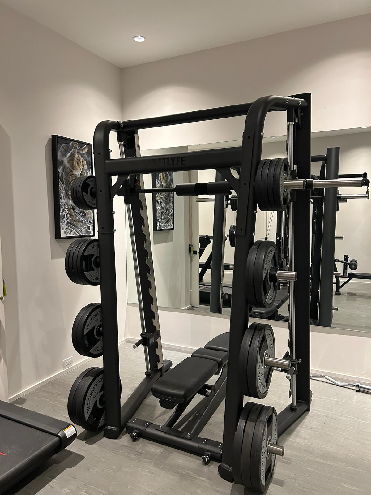Front view of the Smith machine loaded with plates, adjustable bench, and framed wall art in the Kelowna basement home gym.